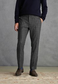 Pantalons à carreaux gris avec une coupe ajustée, fabriqués en tissu texturé. Associés à des mocassins sombres et à un pull bleu marine, présentés sur un fond neutre.