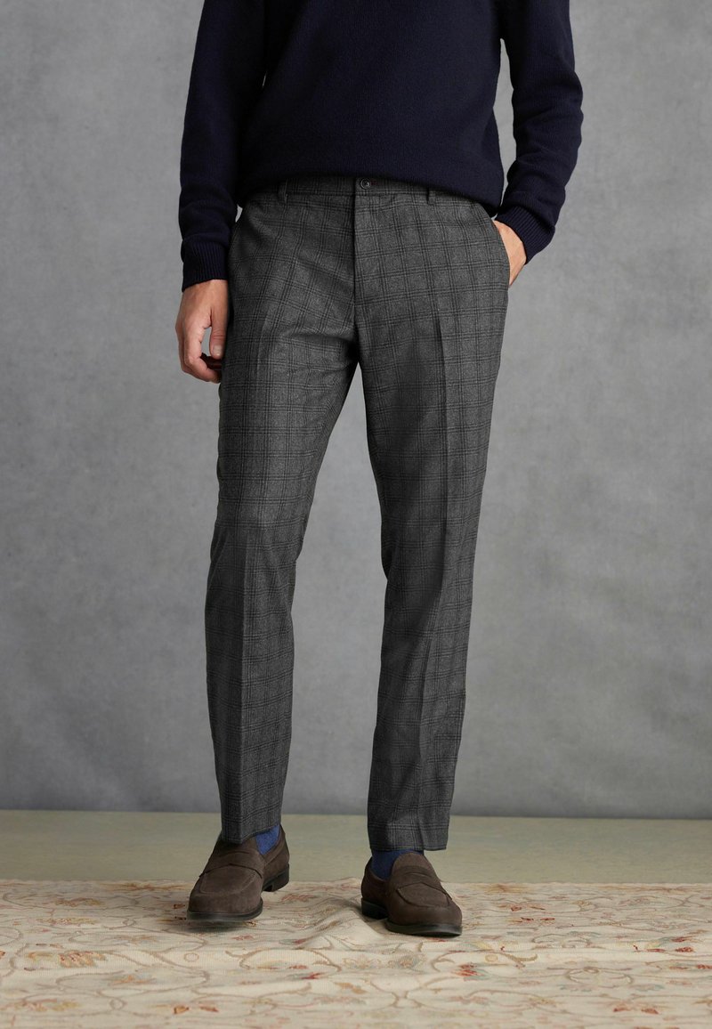Pantalons à carreaux gris avec une coupe ajustée, fabriqués en tissu texturé. Associés à des mocassins sombres et à un pull bleu marine, présentés sur un fond neutre.