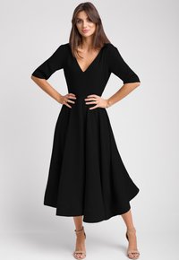 Czarna midi sukienka z dekoltem w kształcie litery V, rękawami o długości trzech ćwierci oraz rozkloszowanym dołem. Wykonana z gładkiego materiału, cechuje się dopasowaną talią i delikatnym drapowaniem.