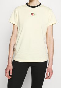 Żółta koszulka z krótkim rękawem z czarnym dekoltem, z kolorową grafiką owoców na piersi. Wykonana z miękkiego materiału bawełnianego.