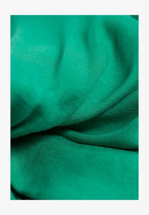 Tissu vert avec une texture lisse et un tissage diagonal fin. Le matériau est drapé, mettant en valeur sa douceur et sa couleur vibrante.