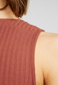 Haut sans manches côtelé couleur rouille avec une surface texturée, doté d'un col rond et d'une coupe douce et ajustée, présenté en vue d'épaule.