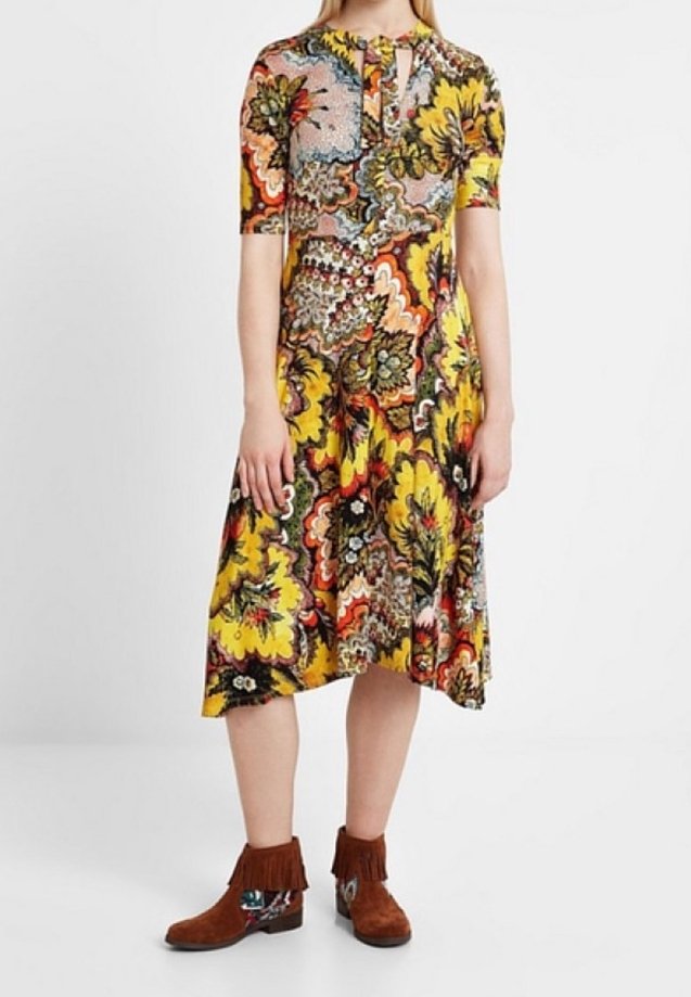 Blommönstrad klänning med korta ärmar, nyckelhålsringning och flödande kjol i gult, rött, grönt och svart; kombinerad med bruna fransboots.