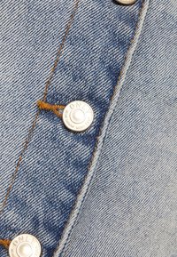 Gros plan sur un tissu en denim bleu avec des boutons argentés et des coutures orange sur un vêtement.