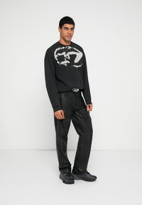 Juodas džemperis su dideliu šviesiai pilku grafiniu atspaudu, derinamas su juodomis odinėmis kargo kelnėmis su kišenėmis ir juodais sportbačiais.