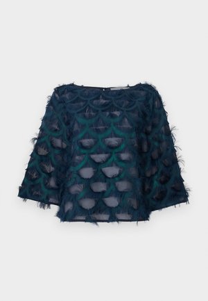 Haut bleu marine en tissu transparent et texturé, présentant des motifs circulaires superposés et des accents frangés. Coupe ample avec des manches trois-quarts.