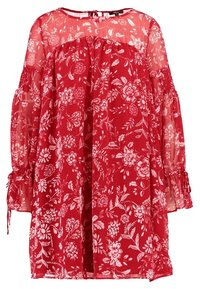 Blouse rouge à fleurs avec un tissu transparent, des manches bouffantes longues et des accents froncés au niveau du col et des poignets. Présente des motifs de fleurs blanches.