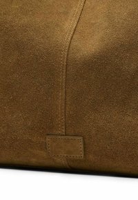 Bruin suède materiaal met een gladde textuur, voorzien van een centrale naad en een rechthoekig leren label dat aan de onderkant is gestikt.