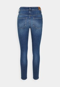 Vaqueros skinny de denim azul mostrados desde atrás con dos bolsillos traseros y una etiqueta de marca marrón en la cinturilla.