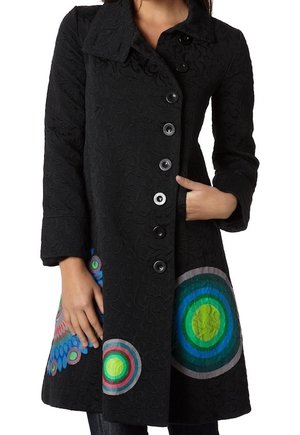 Zwart getextureerde jas met kleurrijke cirkelvormige patronen bij de zoom, voorzijde met knopen, brede kraag, één hand in de zak, gedragen door een staand persoon.