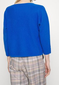 Kungligt blå ribbad stickad tröja med trekvartsärmar och rundad nederkant. Matchas med rutiga byxor som har flera färger och mönster.