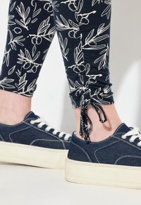 Leggings blu con motivo di rami d'ulivo bianchi e polsini arricciati, abbinati a sneakers in denim blu con lacci bianchi e suola crema.