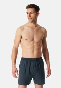 Boxers pour hommes en bleu marine, fabriqués en tissu doux avec une taille élastique, une braguette boutonnée et une coupe décontractée. Texture lisse, design minimal.