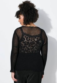 Svart tröja med en genomskinlig, mönstrad rygg som har ett leopardmönster. Långa ärmar med scallopedkanter och strukturerat stickat tyg.