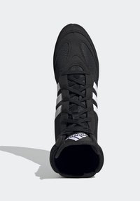 Musta urheilukenkä, jossa on verkkomateriaalia yläosassa, kolme valkoista sivuviivaa, nauhakiinnitys ja pehmustettu nilkkaosa. Sisältää brändilokin kielen kohdalla.