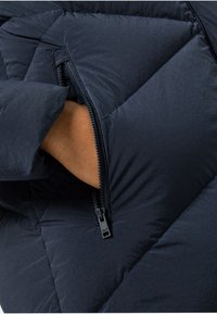 Puffjacke in Dunkelblau mit gesteppter Optik und seitlicher Reißverschlusstasche. Der Stoff wirkt glatt mit einem leichten Glanz.