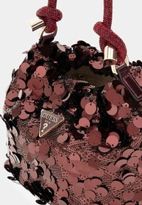 Borsa a tracolla rossa in paillettes con superficie testurizzata, decorata con paillettes tonde e un logo Guess triangolare sul davanti. Due manici intrecciati.