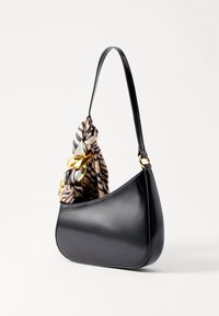 Μαύρη δερμάτινη τσάντα με καμπυλωτό σχήμα, διαθέτει χερούλι από υφασμάτινη με μοτίβα δεμένο σε κόμπο και χρυσά μεταλλικά στοιχεία.