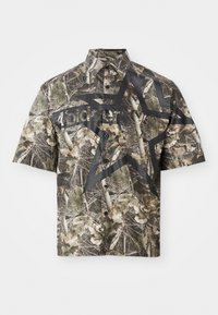 Cămașă cu mânecă scurtă, purtată cu un model camuflat, având un grafic mare cu o stea neagră și text pe față, cu guler clasic și închidere cu nasturi.