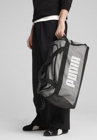 Sac de sport en tissu gris avec un grand logo blanc "PUMA", des accents noirs, des poignées doubles et un fond en maille pour la ventilation.