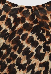 Tkanina s uzorkom leopardove točke, koja ima teksturiranu, meku završnu obradu; prikazuje hrabre crne i smeđe točke na bež pozadini, s fluidnim draperijama.