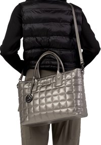 Sac à main matelassé en argent métallique avec deux poignées supérieures et une bandoulière amovible, featuring un charme et un détail de logo.