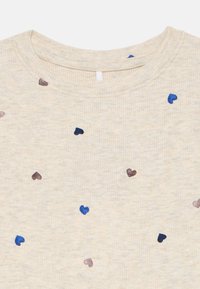 Rippenshirt in Beige mit mehrfarbigen Herzmustern in Braun und Blau, mit Rundhalsausschnitt und einem kurzen Schlaufenetikett auf der Rückseite.