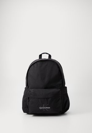 Mochila preta de nylon com forma arredondada, bolso frontal com fecho e pega no topo. Apresenta o logótipo Calvin Klein em branco na parte frontal.