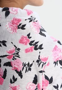 Tessuto bianco con un motivo floreale che presenta rose rosa e foglie nere, texture morbida e design aderente nella scollatura.