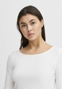 White ribbed long-sleeve top with a wide neckline, smooth texture, and fitted silhouette, featuring subtle vertical stripes.