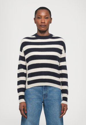 Mørkeblå og hvitstripet genser laget av ribbestrikket stoff, med rund hals og lange ermer, kombinert med blå denimjeans.
