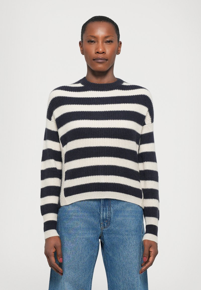 Pull rayé bleu marine et blanc en maille côtelée, avec un col rond et des manches longues, assorti à un jean en denim bleu.