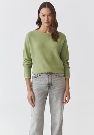 Hellegrüner, gerippter Rundhalspullover mit langen Ärmeln, kombiniert mit hoch geschnittenen, ausgewaschenen grauen Jeans, die eine lockere Passform und subtile Textur präsentieren.