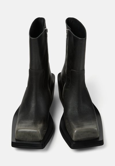Schwarze Lederstiefel bis zur Mitte der Wade mit quadratischen Zehen, Seitenreißverschlüssen und dicken, flachen Sohlen auf weißem Hintergrund.