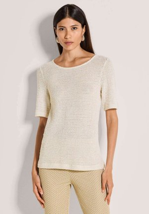 Cremefarbenes, kurzärmeliges, strukturiertes Strickoberteil mit weitem Rundhalsausschnitt, kombiniert mit beigen gemusterten Hosen mit Fischgrätmuster.