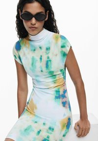 Robe ajustée sans manches blanche avec des motifs abstraits verts, bleus et jaunes. Col haut ; tissu lisse et extensible ; design minimaliste.