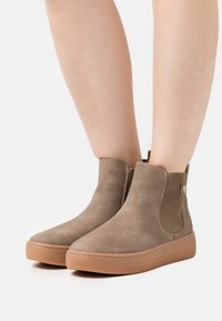 Bottes cheville en daim beige avec panneaux latéraux élastiques et semelles en caoutchouc. Bout arrondi et détails cousus. Tige texturée et design plat.