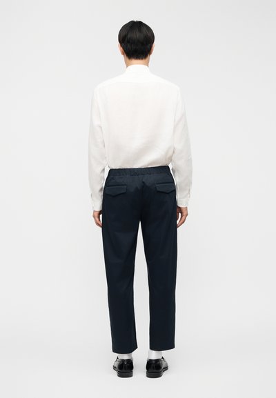 Σκούρο μπλε παντελόνι με άνετη εφαρμογή και ελαστική μέση, με δύο πίσω τσέπες, συνδυασμένο με λευκό πουκάμισο μακρυμάνικο.