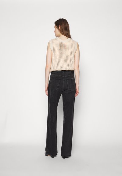 Light beige knit sleeveless top with a loose weave, paired with high-waisted black wide-leg jeans featuring back pockets and minimal stitching.