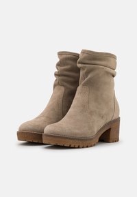 Beige Wildleder-Ankle Boots mit einem schlappen Design, runder Zehenpartie und 5 cm Holzblockabsatz. Genähte Akzente und strukturierte Sohle für besseren Halt.