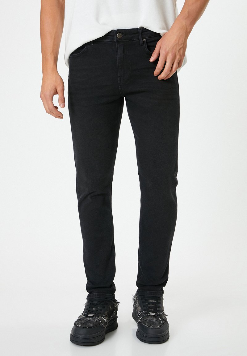 Jeans negros ajustados con una textura suave y diseño de cinco bolsillos, combinados con deportivas oscuras que presentan acentos de tela y cordones en contraste.