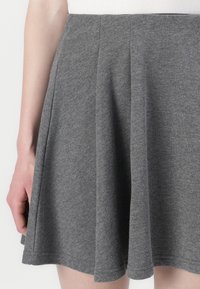 Jupe grise évasée en tissu doux, avec des plis et une texture lisse, dotée d'une taille. Se termine au-dessus du genou.