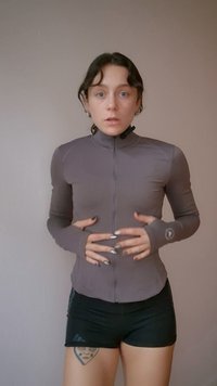 Garām piedurknēm, piegulošs sporta tops noklājuma violetā audumā ar augstu apkakli un rāvējslēdzēju. Kombinēts ar melniem šortiem ar sānu svītrām.