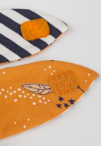 Stoffstücke in gestreiftem Marineblau und Weiß sowie Orange mit Mustern von Blättern und Sternen. Jedes Stück hat einen strukturierten gelben Fleck.