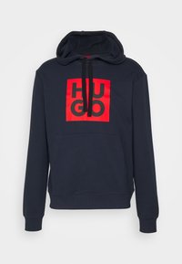 Sweat à capuche bleu marine avec poche avant et cordons noirs, avec un graphique carré rouge comportant des lettres noires en gras formant le mot HUGO.