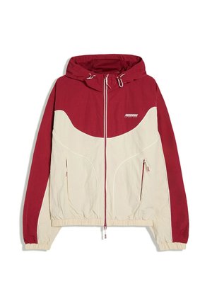 Jachetă tip windbreaker cu glugă, în roșu și bej, cu fermoar frontal, manșete și tiv elastice, și două buzunare laterale cu fermoar.