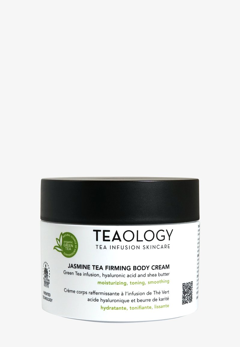 Couvercle noir et pot blanc de la crème corporelle raffermissante au thé jasmin de Teaology. L'étiquette présente des illustrations de thé vert, avec des informations pertinentes sur le produit et un code QR.