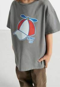 Hallhalli puuvillane T-särk, millel on suur ja värvikas graafika propelleriga mütsist, millel on silt "AMV lasteklubi" sinises kirjas. Lühikesed varrukad, mugav lõige.