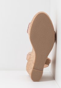 Sandale compensée avec une tige synthétique rose clair, semelle en liège et semelle extérieure en caoutchouc texturé. Comprend des sangles réglables pour un maintien sécurisé.