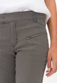 Zwart-witte geblokte broek gemaakt van gestructureerde stof, met een voorzak en een aansluitende tailleband. Close-up weergave toont de patroon details.
